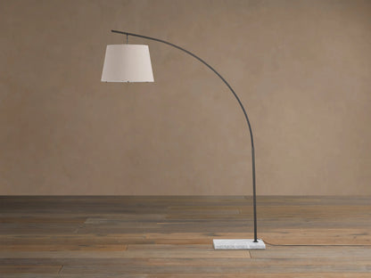 Tadeo Floor Lamp: dark arcing frame, light linen drum shade, white marble base, on wooden floor against a warm wall.