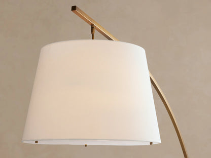 Tadeo Floor Lamp: stylish arched brass floor lamp with a white linen shade and a dark marble base, on a wooden floor.