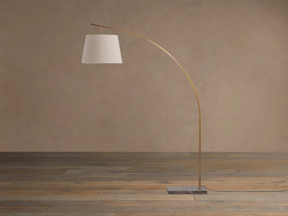 Tadeo Floor Lamp: Arched brass-finished stand, natural linen shade, and espresso marble base on a wooden floor.