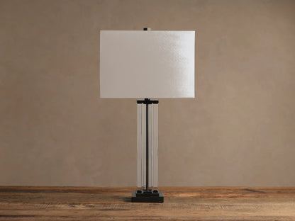 Dawson Table Lamp with glowing white rectangular shade, clear and dark metal base, on a rustic wooden table.