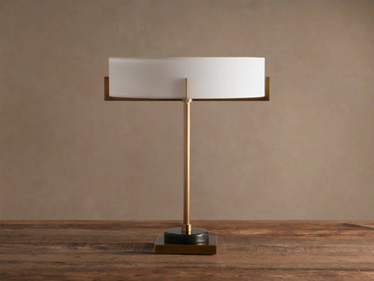 Frederic Table Lamp with antiqued brass finish, black granite base, and illuminated white linen shade on a wooden table.