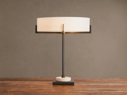 Illuminated Frederic Table Lamp with a bronze frame, white linen shade, and a cream marble disc on a dark square base, on wood.