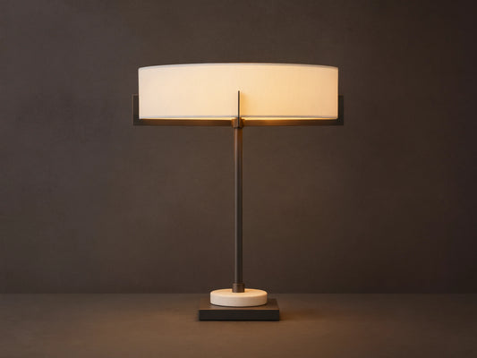 Illuminated Frederic Table Lamp with a bronze frame, white linen shade, and a cream marble disc on a dark square base, on wood.