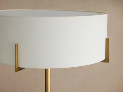 Frederic Floor Lamp: antiqued brass iron pole, white linen shade, and black granite base, standing on a wooden floor.