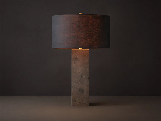 Pyrite Table Lamp with a rectangular base made of dark, shimmering pyrite pieces, topped by a black linen drum shade on a wooden table.