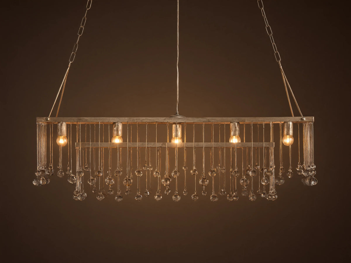Aubrey Rectangular Chandelier with a silver handcrafted iron frame, hanging Italian glass crystals, and five glowing bulbs.