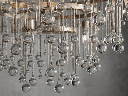 Aubrey Round Chandelier in silver with a large circular iron frame, adorned with cascading hanging glass crystals, suspended from a chain against a neutral wall.