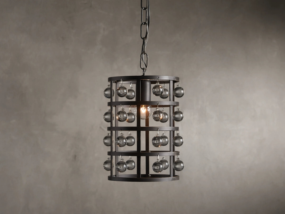 Iron cage pendant with antiqued metallic finish, adorned with Italian crystal spheres, hanging from a chain on a textured wall background.