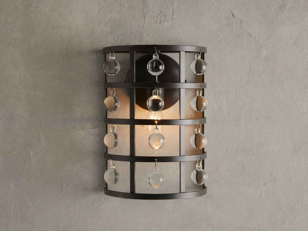 Iron cage sconce with antiqued metallic finish and Italian crystal spheres, mounted on a textured wall, lit from within.