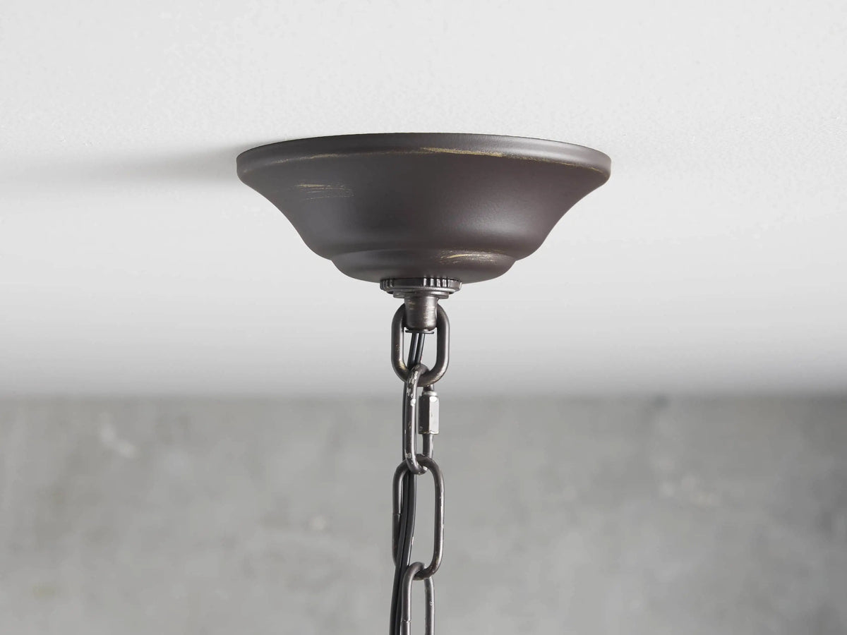 Aubrey Round Chandelier with a dark iron frame, five exposed bulbs, and hanging clear glass orbs against a textured gray wall.