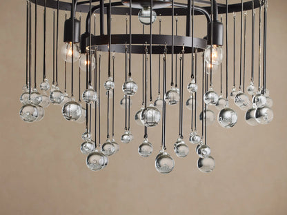 Aubrey Flush Mount: Black iron frame with clear glass spheres suspended by thin rods at varying lengths, against a beige ceiling.