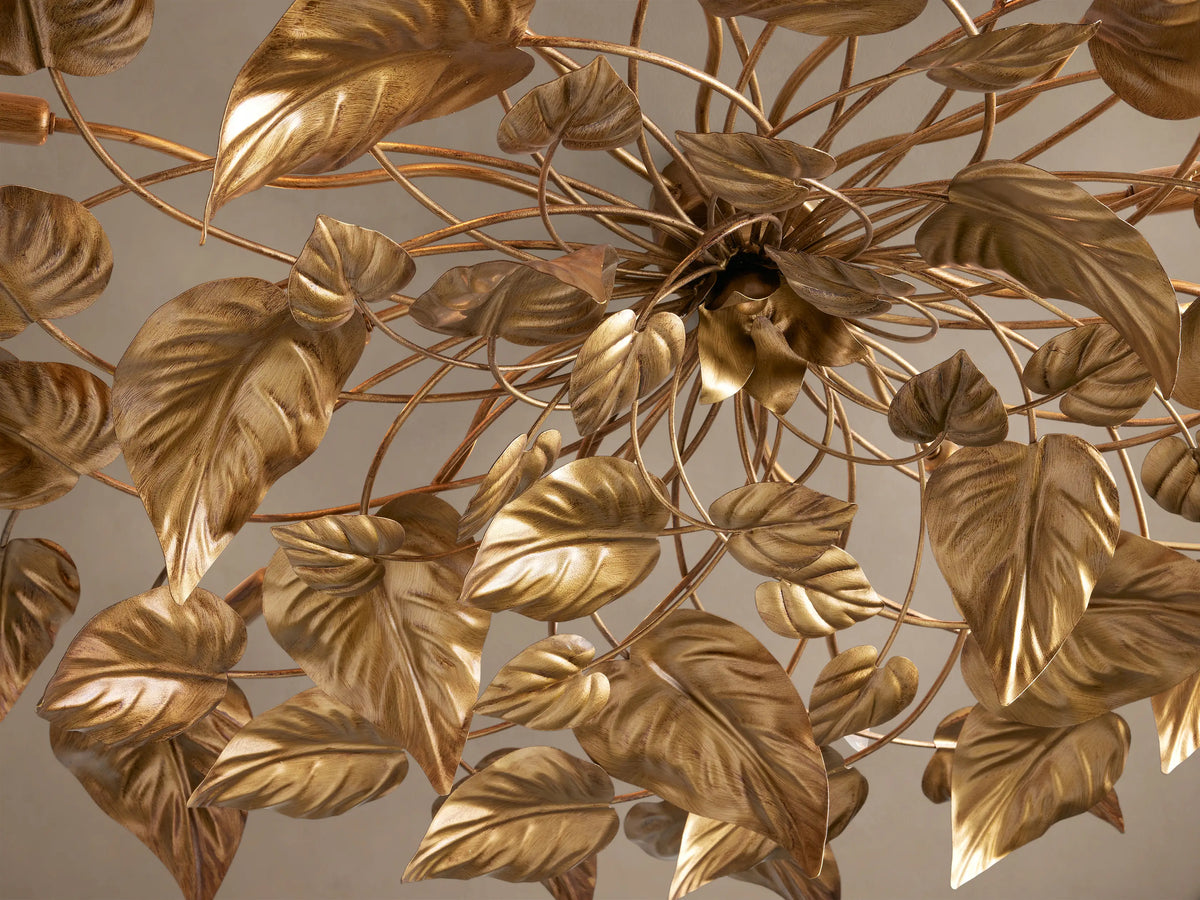 Ninfea Flush Mount: An antiqued gold iron ceiling light with numerous metallic leaves and small bulbs, against a beige ceiling.