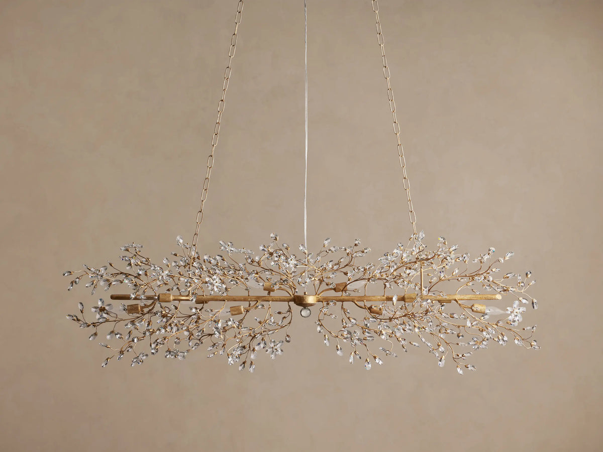 Fiore Linear Chandelier, golden finish, adorned with delicate branching crystal leaves, exposed candelabra bulbs, suspended by chains.