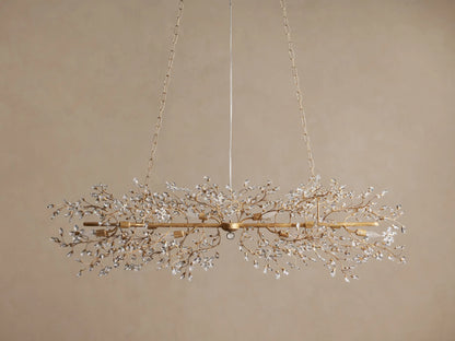 Fiore Linear Chandelier, golden finish, adorned with delicate branching crystal leaves, exposed candelabra bulbs, suspended by chains.