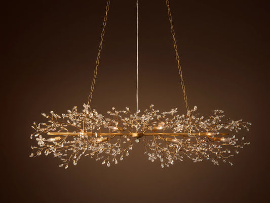 Fiore Linear Chandelier, golden finish, adorned with delicate branching crystal leaves, exposed candelabra bulbs, suspended by chains.