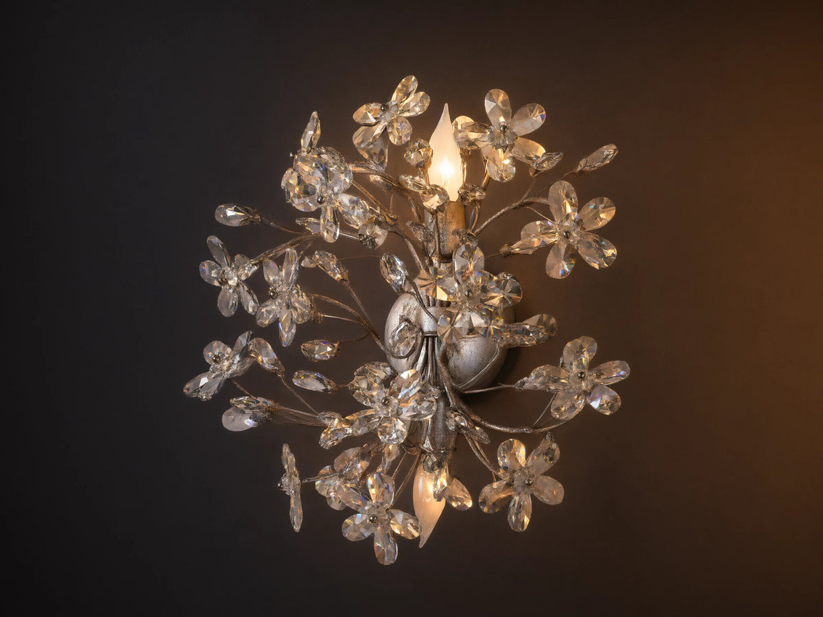 Antiqued silver Fiore Sconce, wall-mounted, featuring numerous clear crystal flowers & buds, with two lit candelabra bulbs.