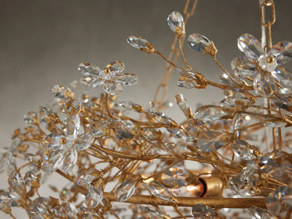 Close-up of Fiore Crown Chandelier: intricate gold branches with sparkling clear crystal flowers & buds. Warm light bulb glow.