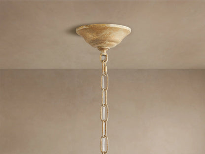 Close-up of Fiore Crown Chandelier's antiqued gold canopy & chain hanging from a light brown ceiling.