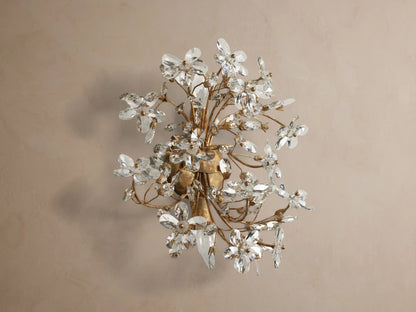 Fiore Sconce: Elegant gold iron sconce with clear crystal flowers, sparkling and glowing with warm light, mounted on a neutral wall.