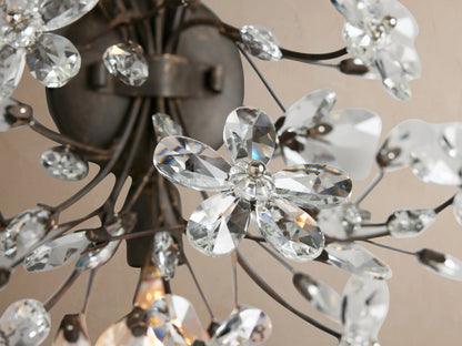 Fiore Sconce: Floral wall light with dark bronze branches and sparkling clear crystal flowers, mounted on a beige wall.
