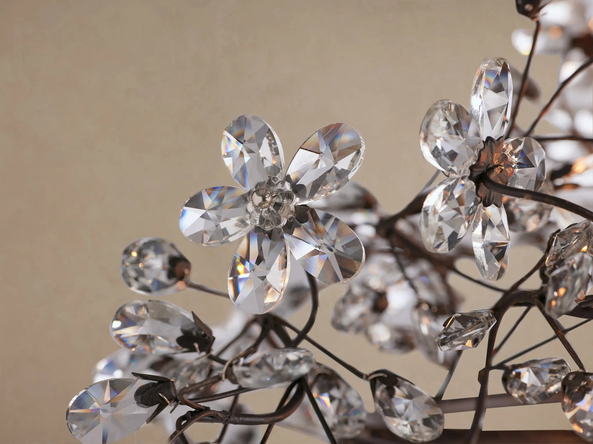 Fiore Linear Chandelier, dark metal frame with many clear crystal flowers & buds, suspended by chains against a plain background.