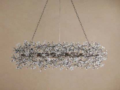 Fiore Oval Chandelier: horizontal oval dark metal frame with intricate branch-like design, adorned with numerous clear crystal blossoms, illuminated.