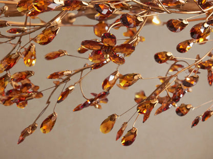 Fiore Crown Chandelier: Golden circular chandelier adorned with numerous sparkling amber leaf-shaped pieces, hanging from golden chains.