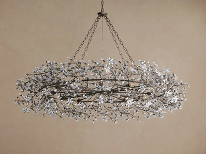 Fiore Crown Chandelier. Oval, dark metal frame covered in sparkling clear crystal flowers, suspended by chains on a light brown background.