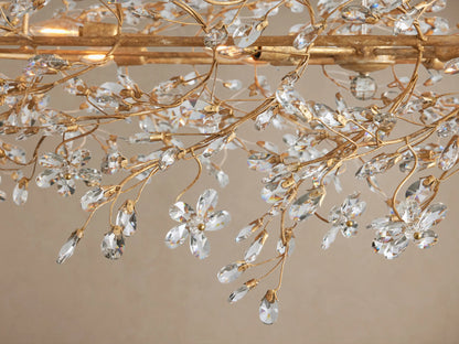 Fiore Oval Chandelier, gold metal frame with intricate branches covered in sparkling clear crystal leaves, hanging from gold chains.