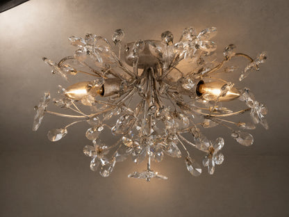 Fiore Flush Mount light fixture with intricate antique silver floral branches adorned with clear crystal flowers and leaves, illuminated.