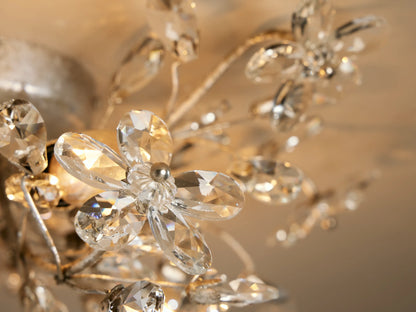 Fiore Flush Mount: Silver-toned metal fixture on ceiling, branching arms, clear crystal flowers & teardrops, two warm candelabra bulbs visible.