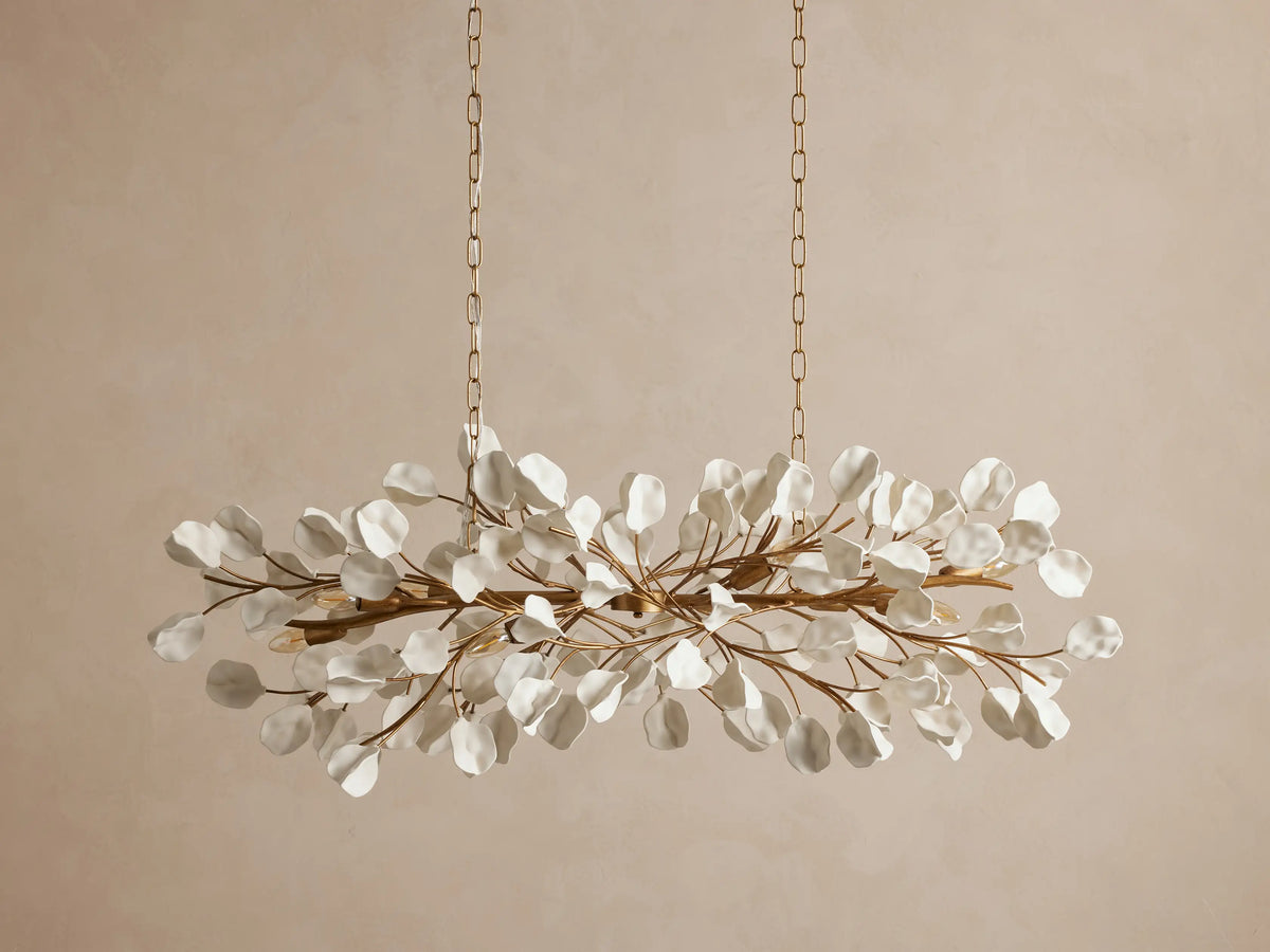 Lunaria Linear Chandelier: horizontal golden fixture with white, translucent leaf-like accents on branches, emitting a warm glow.