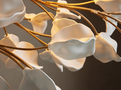 Close-up of Lunaria Linear Chandelier's white ceramic petal-like forms on textured golden branches, with soft warm illumination.