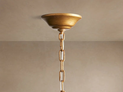 Close-up of the Ninfea Chandelier, showing detailed antiqued gold metal leaves and curved arms against a muted background.