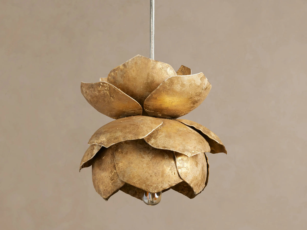 Lorca Pendant: Textured golden floral-shaped light fixture with layered petals, bulb glowing warmly, against a neutral wall.