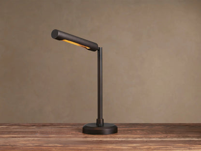 Elih Desk Lamp: Antiqued bronze brass finish, modern design with cylindrical head angled down, emitting warm light on a wooden surface.