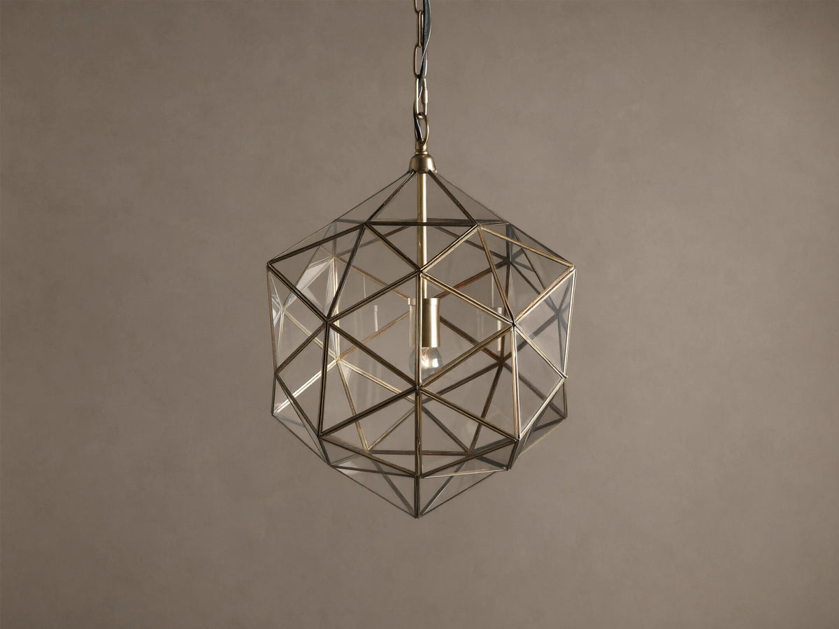 Eliana Lantern Pendant: Geometric brass and clear glass lantern hanging from a black chain, with a light bulb inside.