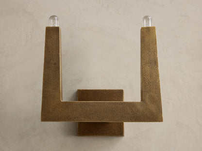 Front view of textured bronze U-shaped wall sconce with two glowing bulbs.