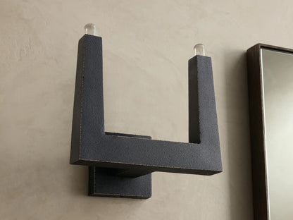 Front view of a dark gray textured U-shaped wall sconce with two clear glass bulbs at the top.