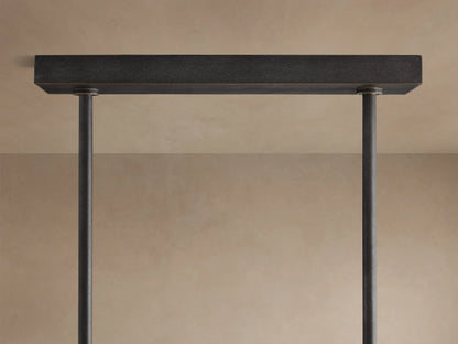Emmet Linear Chandelier, dark textured antiqued brass frame with square arms, glowing filament bulbs visible.