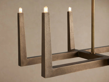 Emmet Linear Chandelier, antiqued brass linear frame with upward-facing light sockets, suspended from two rods against a plain wall.