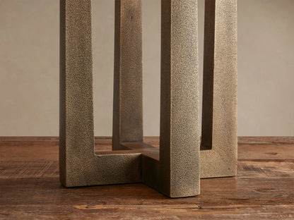 Emmet Table Lamp with a white cylindrical shade & three antiqued brass rectangular supports on a rustic wooden table.