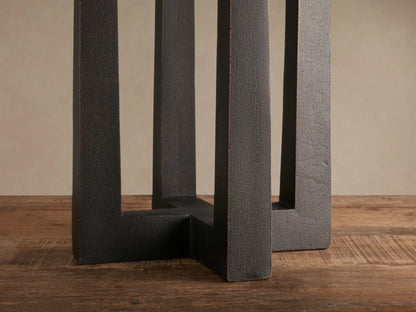 Emmet Table Lamp with white linen shade and dark, textured antiqued brass three-pillar base on a rustic wooden table.