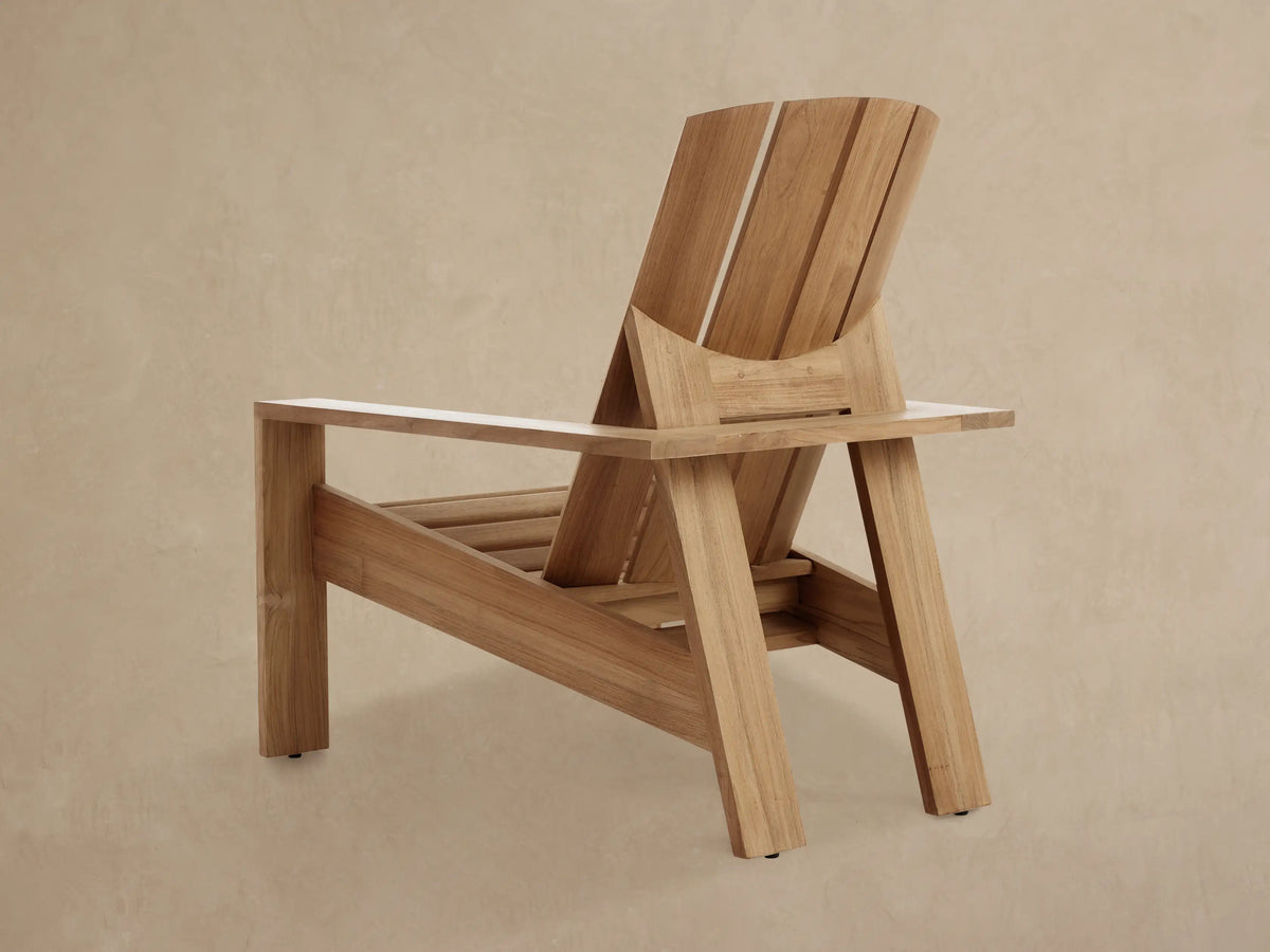 Angled close-up of an Adirondack Outdoor Lounge Chair, showing untreated golden teak wood slats, natural grain, and joinery details.