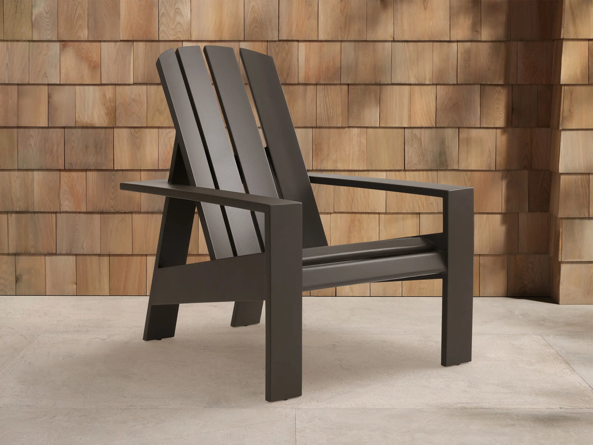 Powder-coated dark bronze Adirondack outdoor aluminum lounge chair, angled against a wooden shingle wall on light pavement.