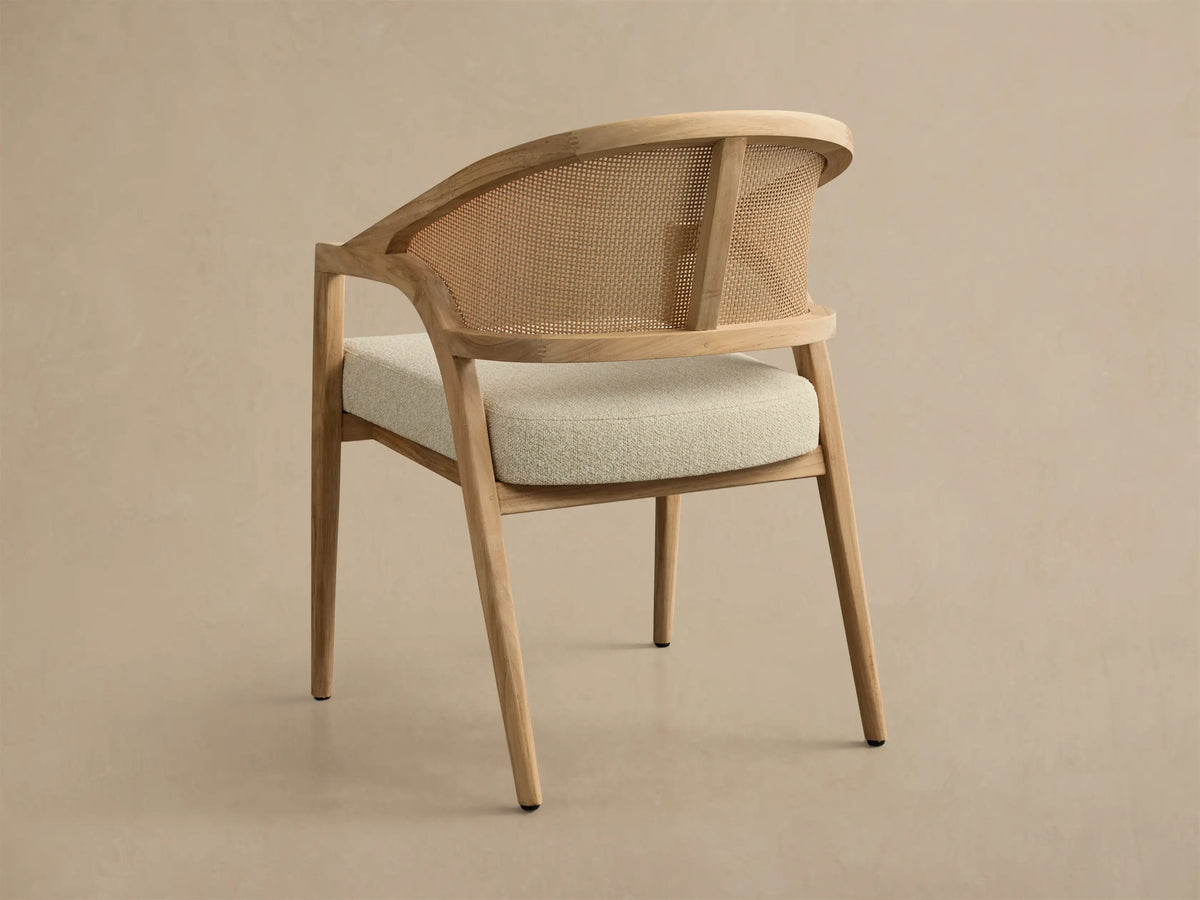 Rear view of the Aimee Outdoor Dining Chair, featuring a light natural teak wood frame, woven caning backrest, and light cream cushion.