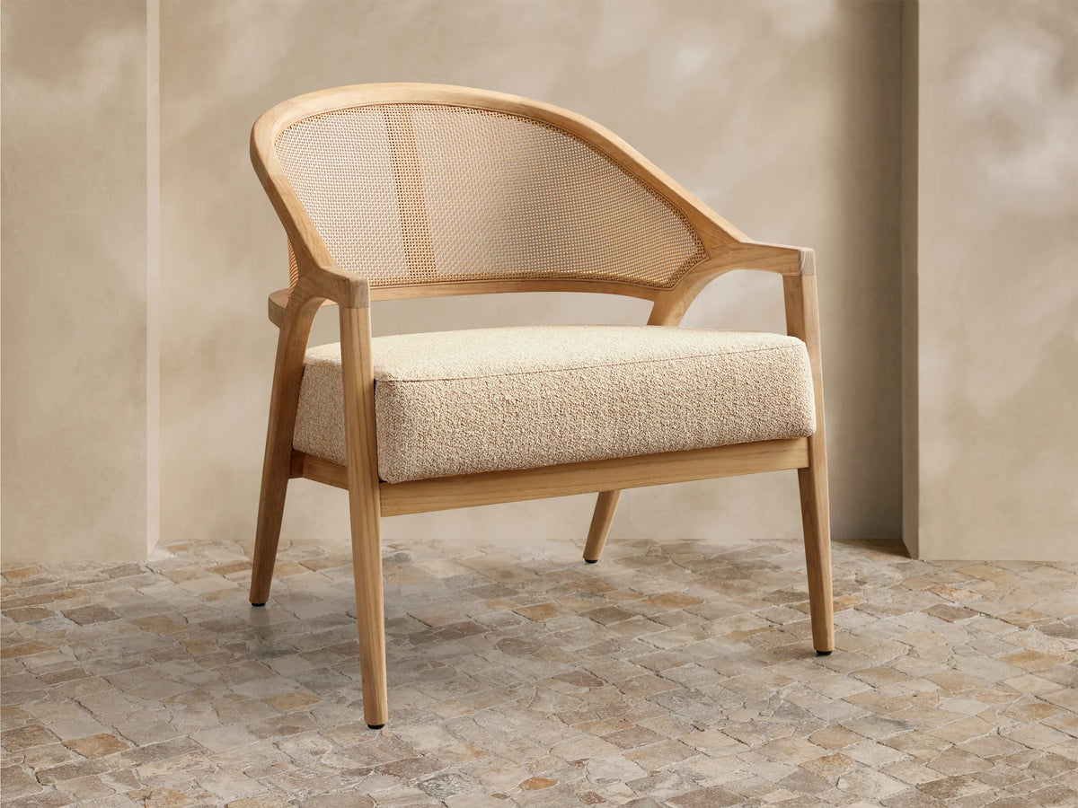 Front view of the Aimee Outdoor Lounge Chair featuring a light teak wood frame, woven resin caning back, and a textured beige cushion.