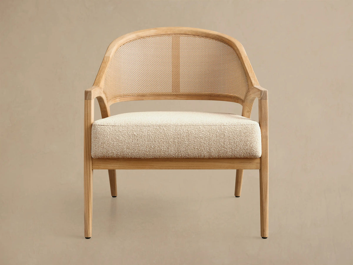 Front view of the Aimee Outdoor Lounge Chair, featuring a light teak wood frame, natural woven caning backrest, and cream textured seat cushion.