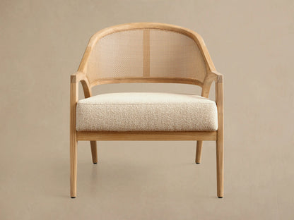 Front view of the Aimee Outdoor Lounge Chair, featuring a light teak wood frame, natural woven caning backrest, and cream textured seat cushion.