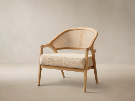 Front view of the Aimee Outdoor Lounge Chair featuring a light teak wood frame, woven resin caning back, and a textured beige cushion.